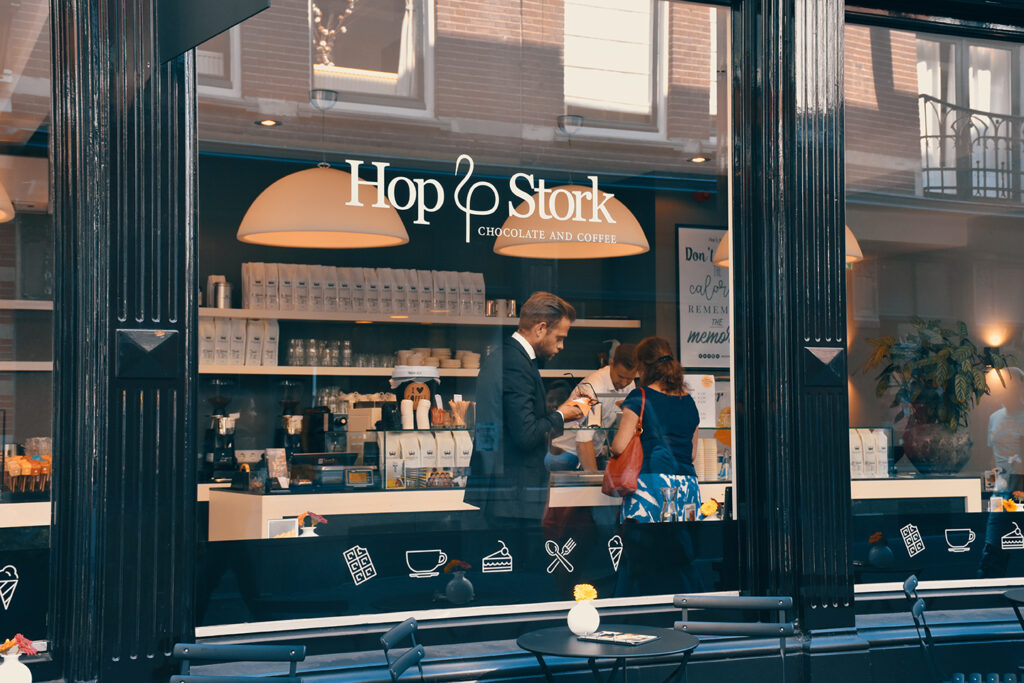 photo from outside of "Hop Stork Chocolate and Coffee" looking into window with customers on line and barista working